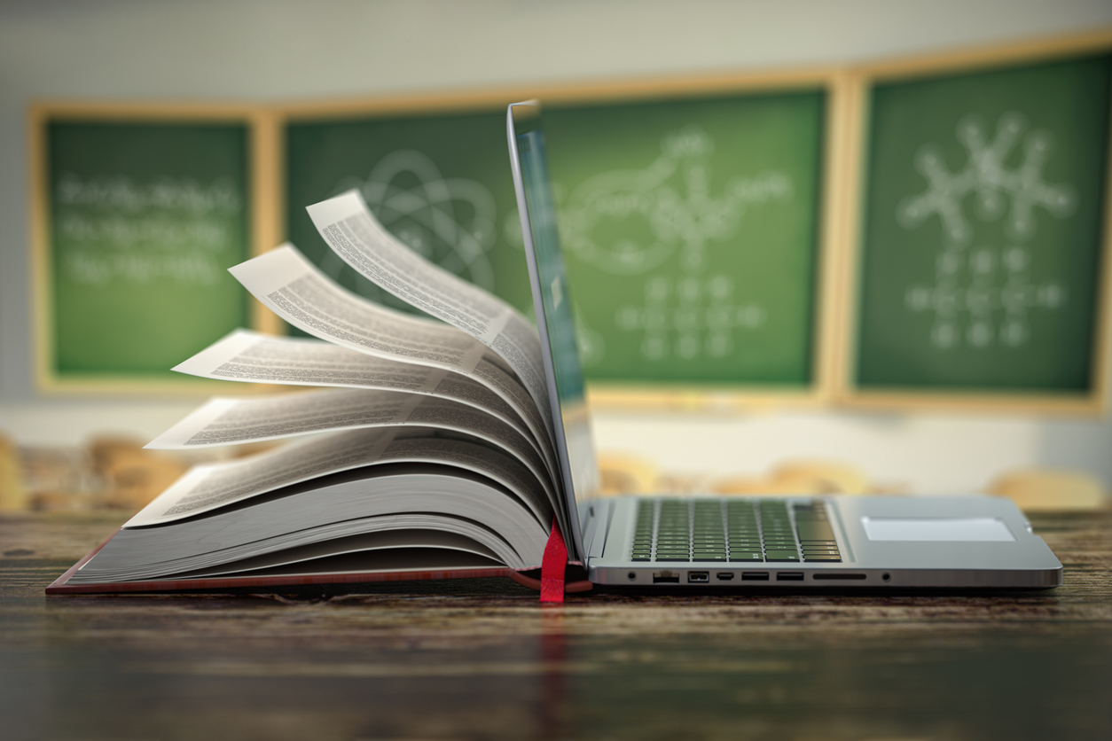 E-learning online education or internet encyclopedia concept. Open laptop and book compilation in a classroom. Blog page for the website. The image depicts an opening book and an open laptop.